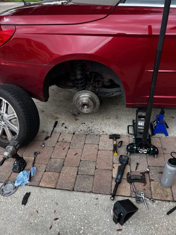 Brake job on a car jacked up in the driveway with tools laid out