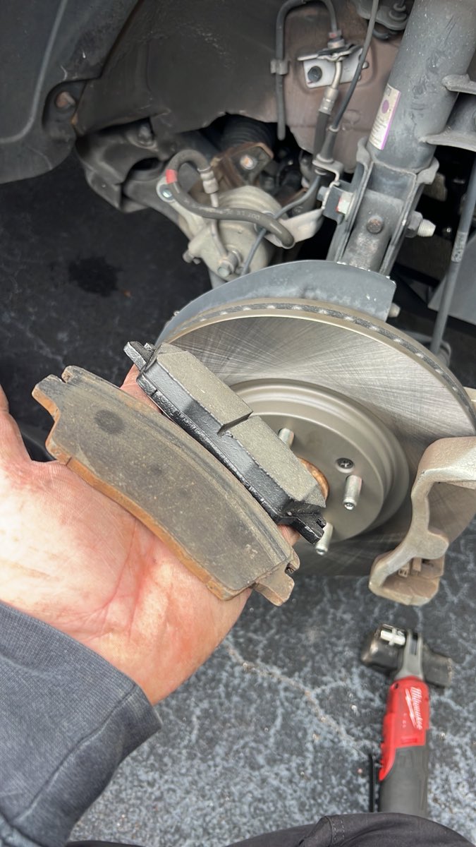 Worn brake pad held next to a freshly serviced brake rotor on a customer's car