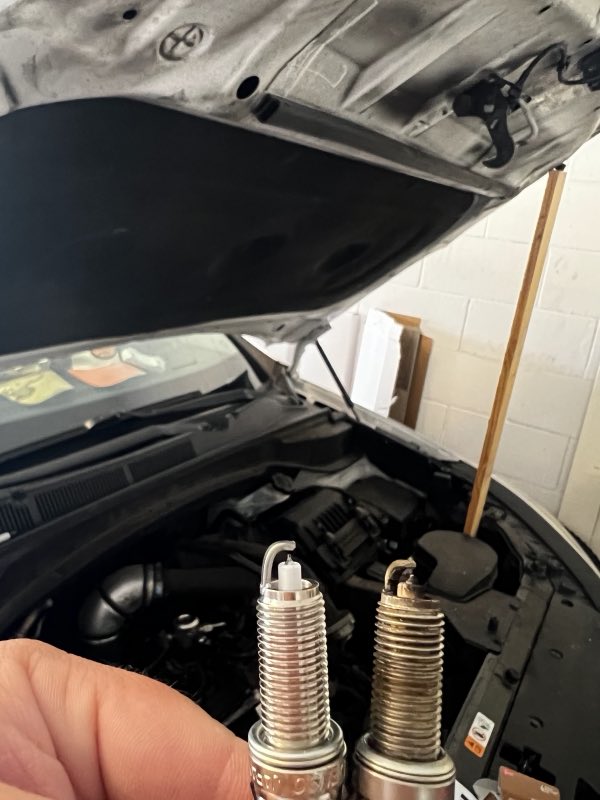 Old and new spark plugs compared during a replacement